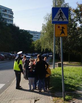 Zdjęcie kolorowe, przedstawiające policjanta ruchu drogowego i dzieci z klasy pierwszej.