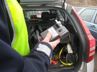 Zdjęcie kolorowe, przedstawiające policjanta ruchu drogowego i urządzenie alco-sensor.